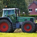 Modernus traktorius žaliame lauke saulėtą dieną, simbolizuojantis kokybišką žemės ūkio techniką.